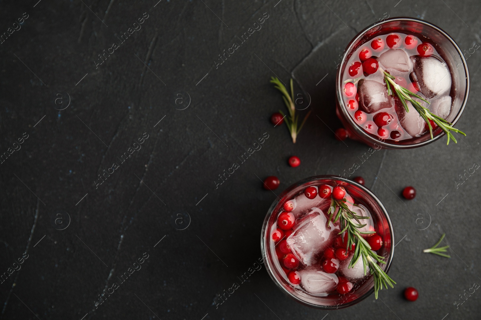 Photo of Tasty refreshing cranberry cocktail with rosemary on black table, flat lay. Space for text