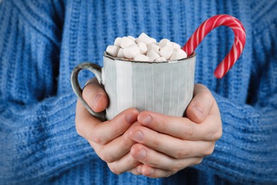 Woman holding cup of delicious hot chocolate with marshmallows and candy cane, closeup