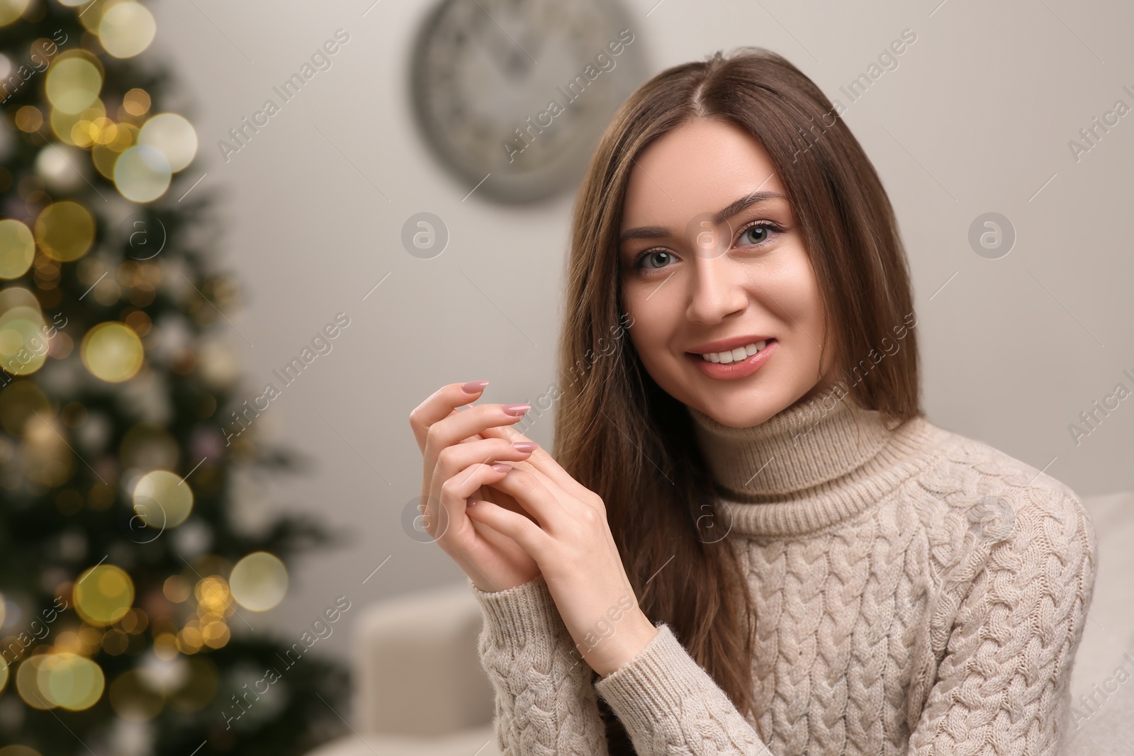 Photo of Beautiful young smiling woman near Christmas tree at home, space for text