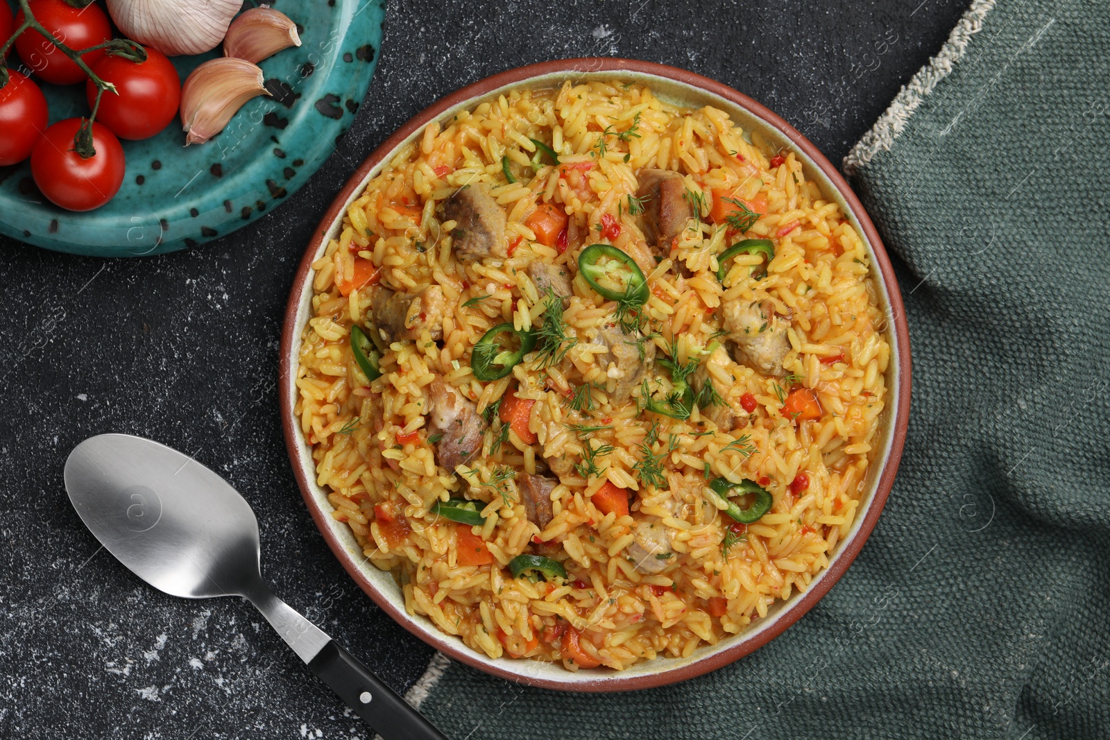 Photo of Delicious pilaf with meat and ingredients on black textured table, flat lay