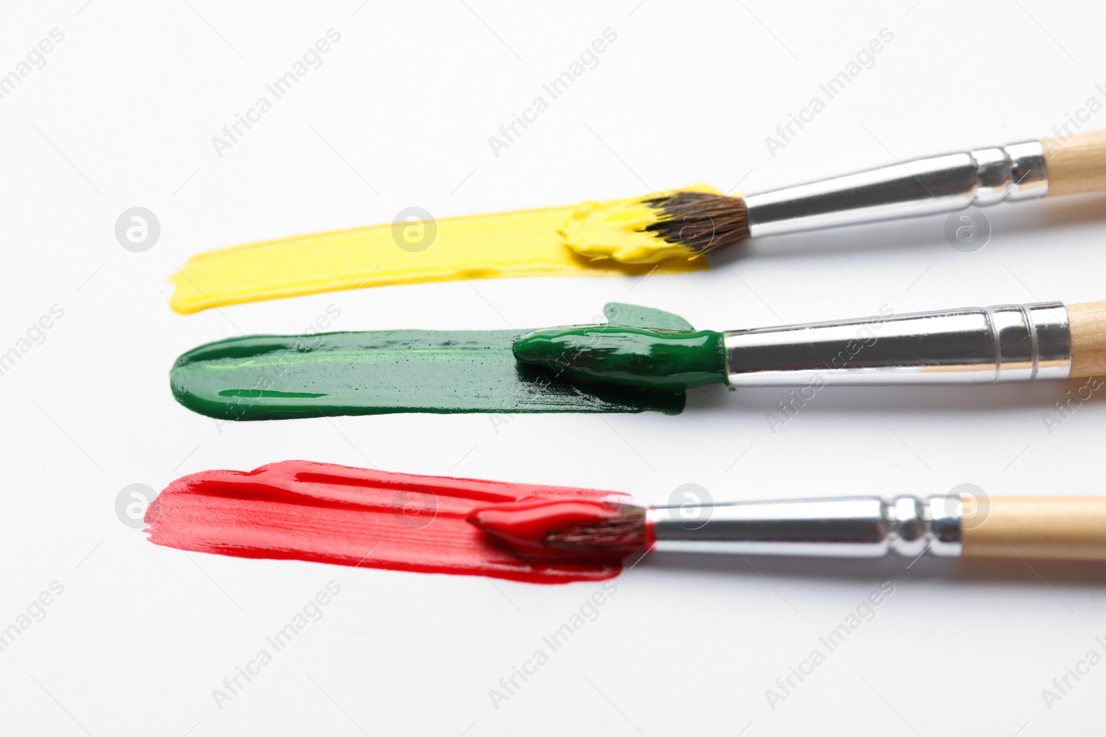 Photo of Brushes with different paints and strokes on white background, closeup