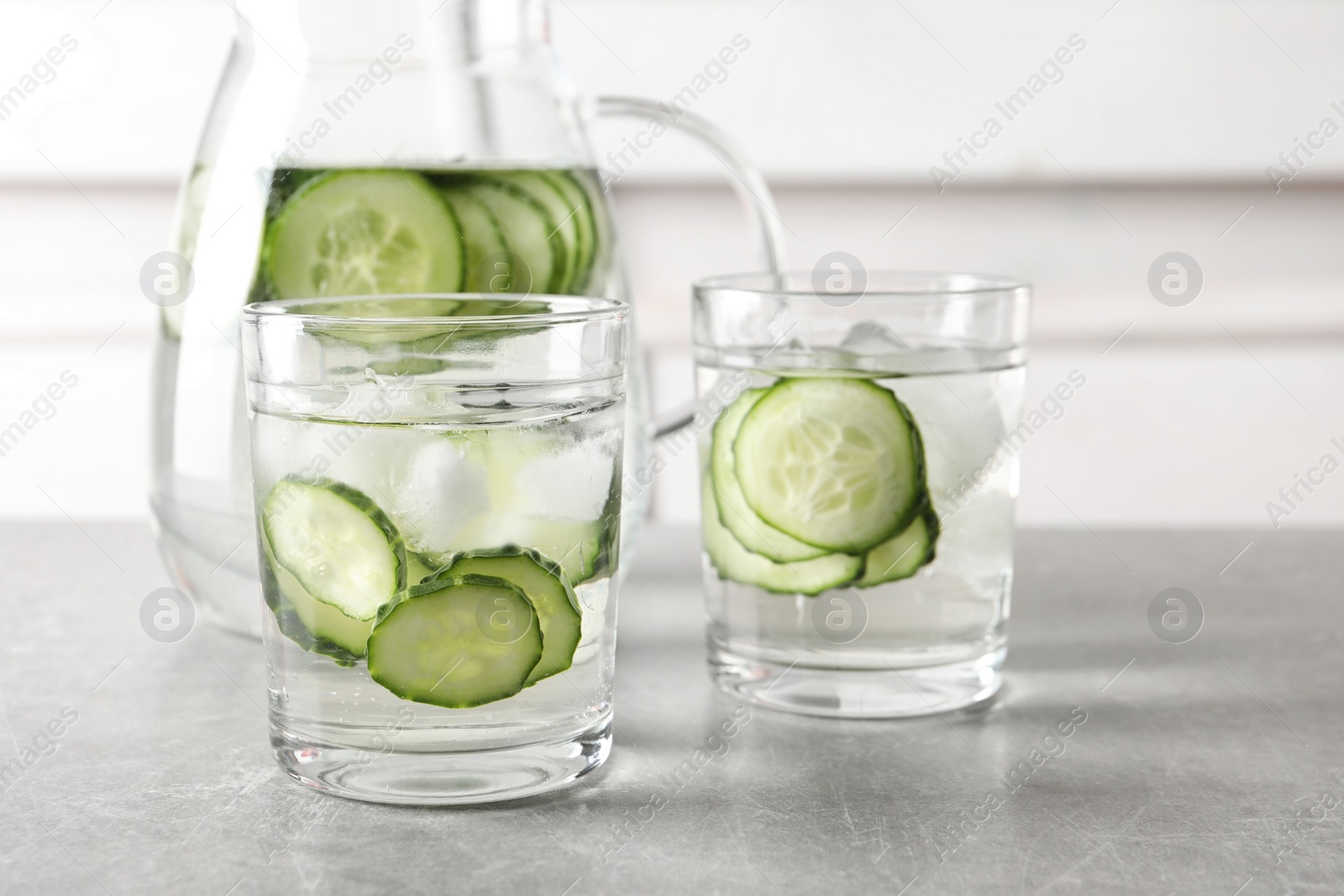 Photo of Glasses and jug of fresh cucumber water on table