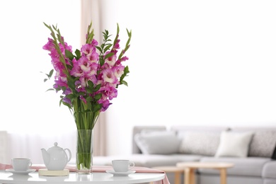 Photo of Vase with beautiful pink gladiolus flowers on wooden table in living room. Space for text