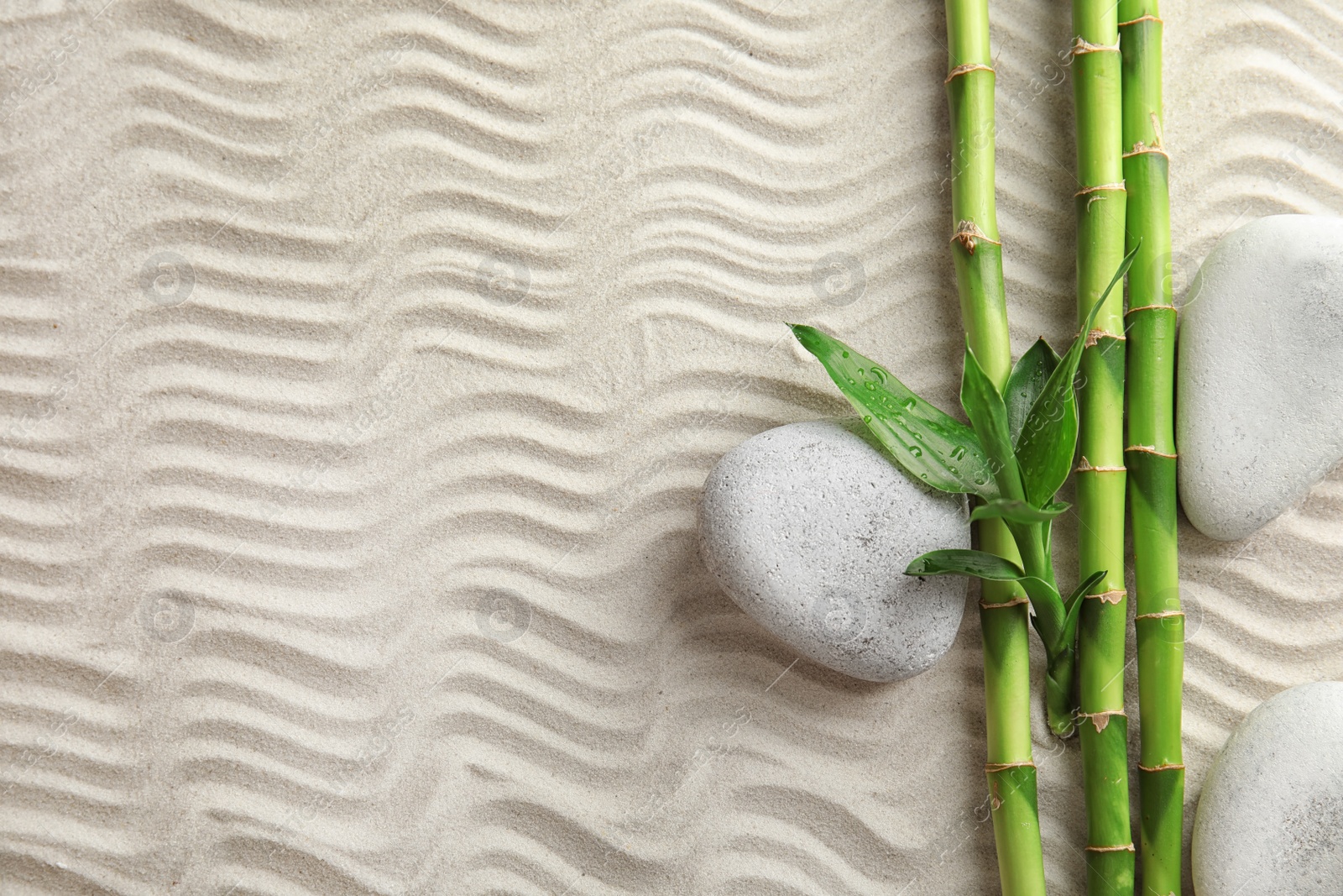 Photo of Bamboo branches with spa stones on sand, top view. Space for text