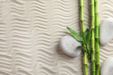 Photo of Bamboo branches with spa stones on sand, top view. Space for text