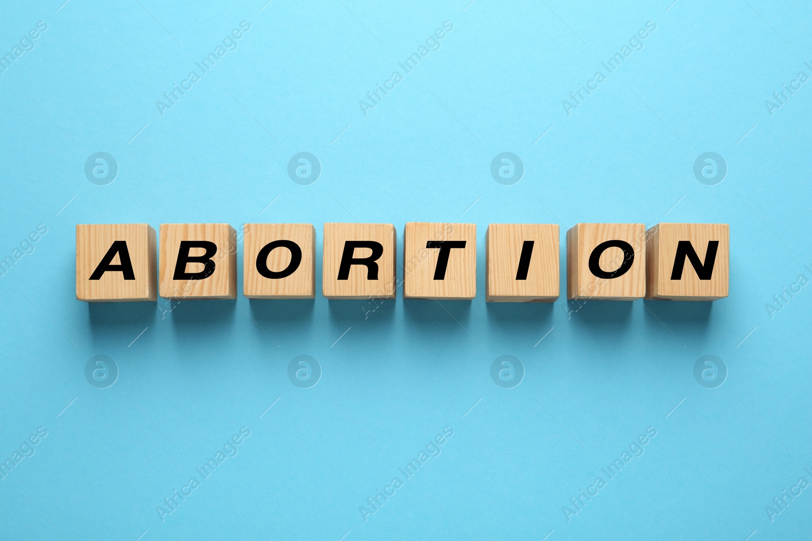 Photo of Word Abortion made of wooden cubes on light blue background, flat lay