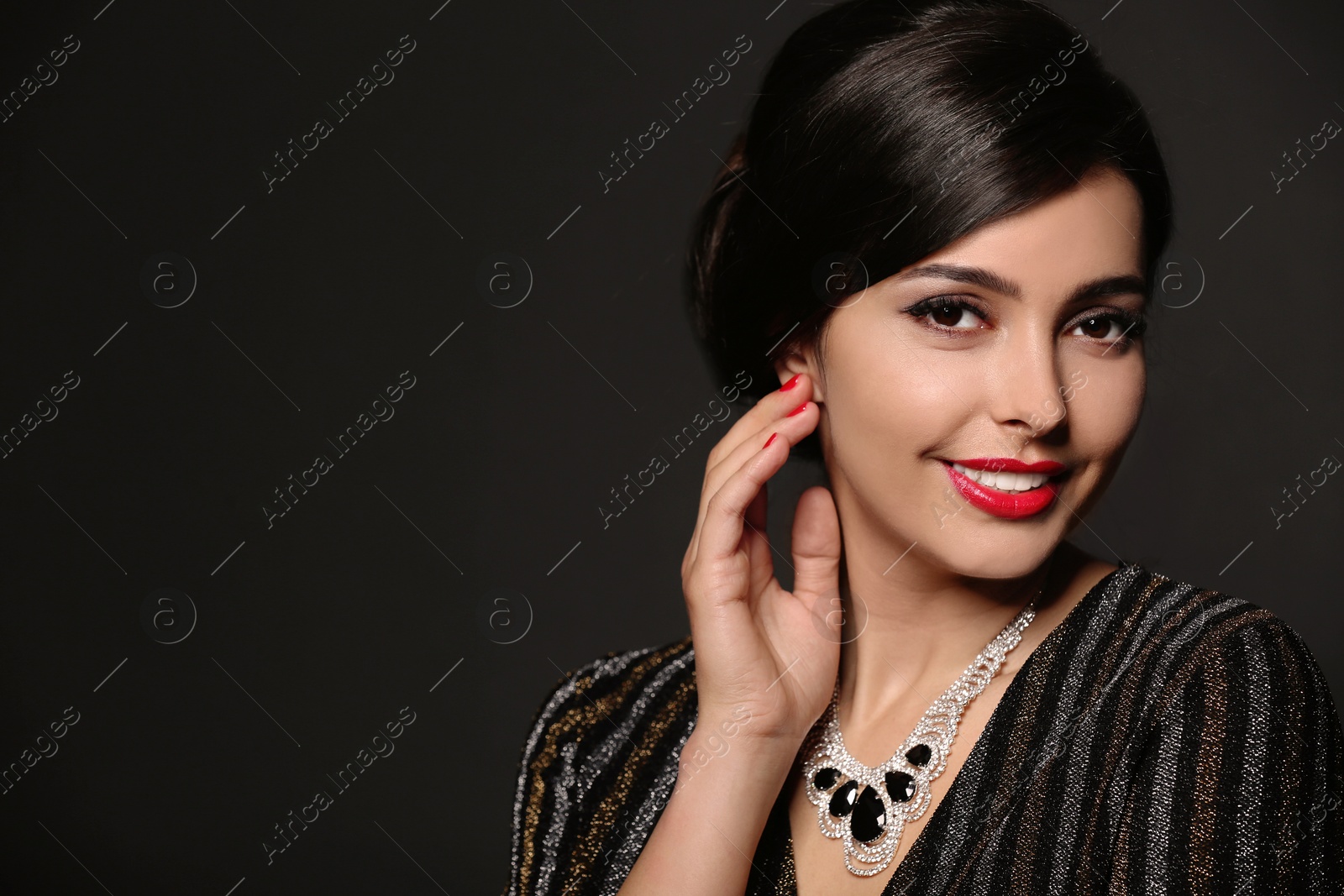 Photo of Beautiful young woman with elegant jewelry on dark background. Space for text