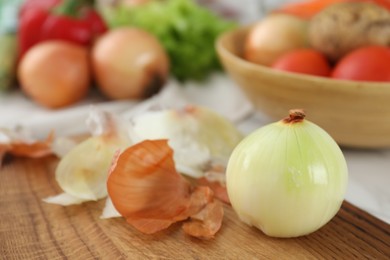 Photo of Wooden board with fresh onion and peels on table, closeup