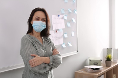 Photo of Teacher with protective mask near board in classroom. Reopening after Covid-19 quarantine