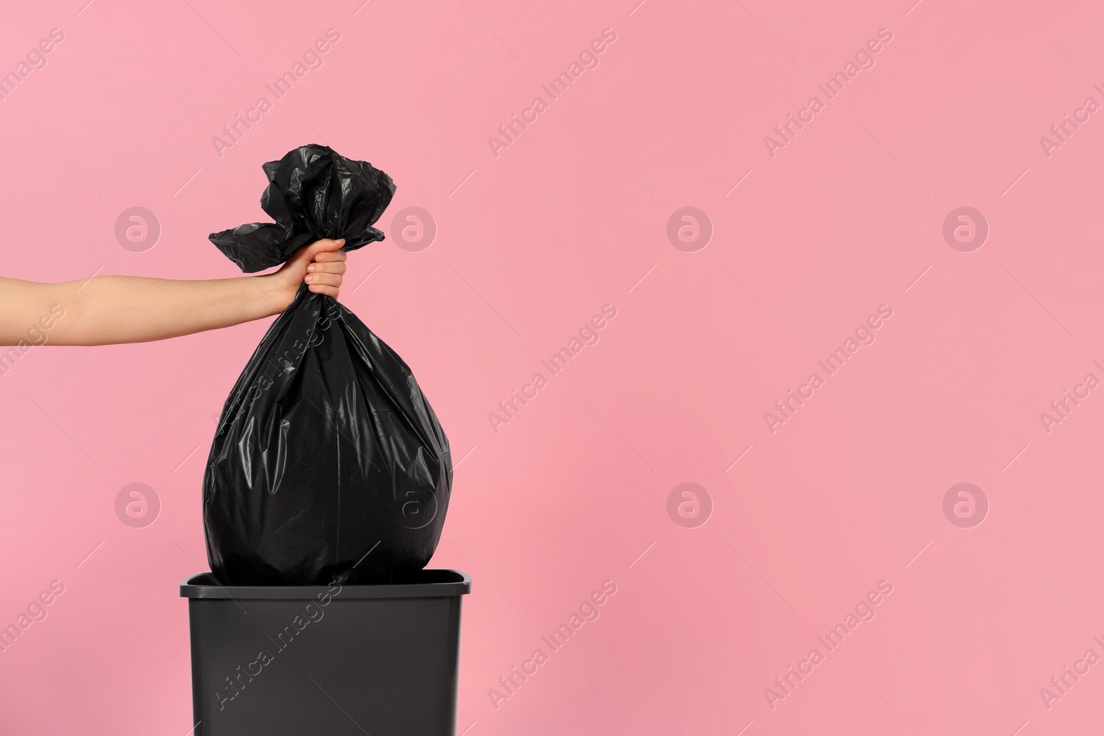 Photo of Woman holding trash bag full of garbage over bucket on pink background, closeup. Space for text