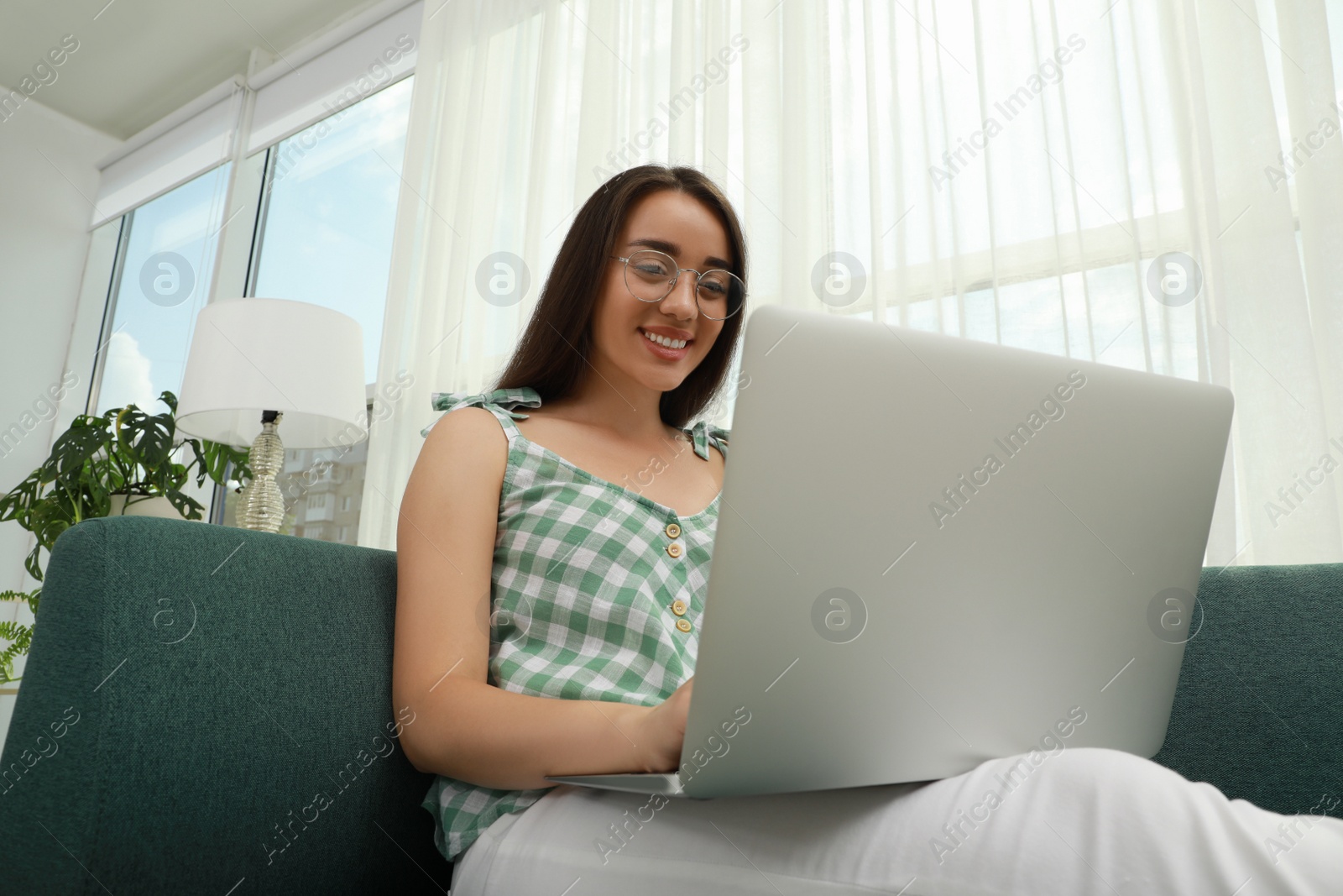 Photo of Young woman using laptop on sofa at home. Internet shopping