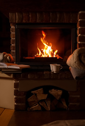 Photo of Knitwear and books near fireplace with burning wood indoors. Winter vacation