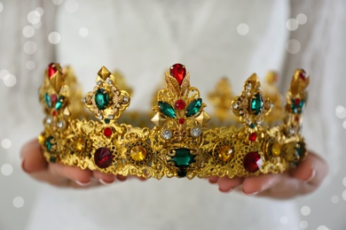 Photo of Woman holding beautiful crown with gems on light background, closeup. Fantasy medieval period