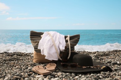 Photo of Beautiful hat with sunglasses, bag and flip flops near sea on pebble beach