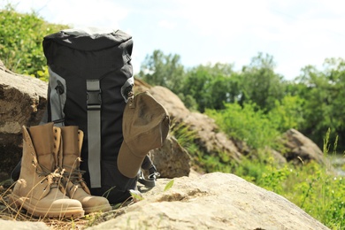 Photo of Backpack and camping equipment on large stone in wilderness. Space for text