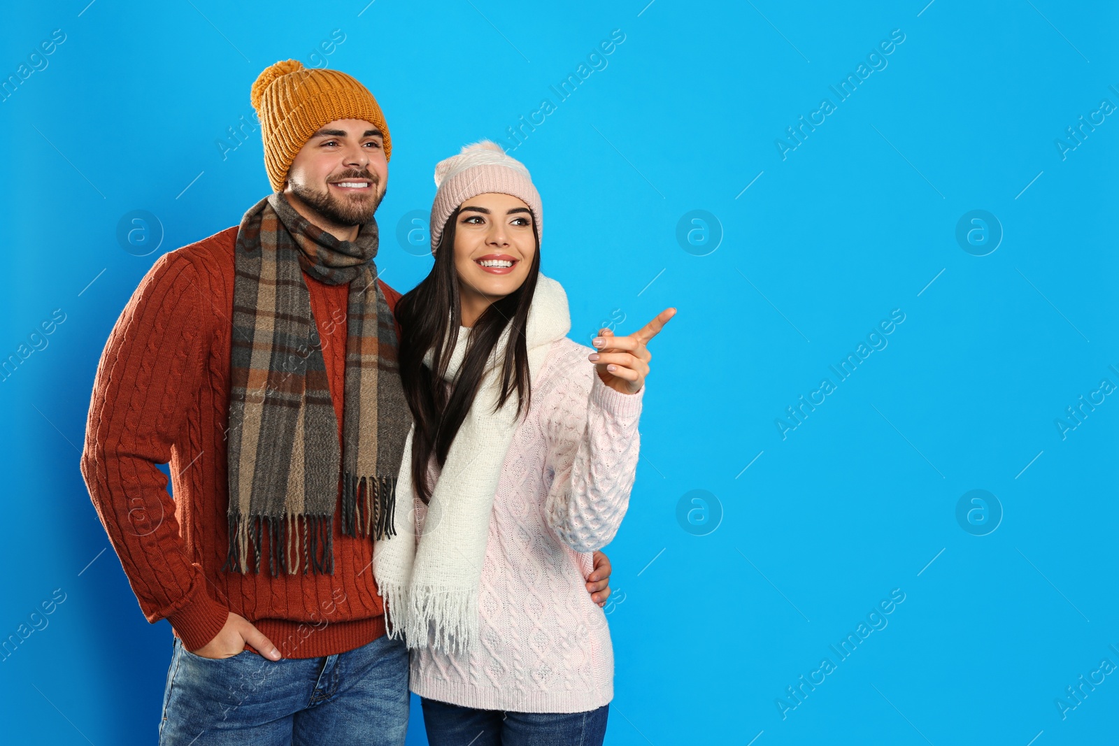 Photo of Happy young couple in warm clothes on blue background, space for text. Winter vacation