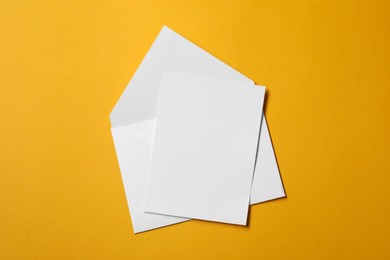 Photo of Blank sheet of paper and letter envelope on orange background, top view