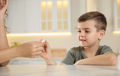 African-American woman giving vitamin pill to little boy in kitchen
