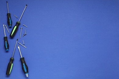 Photo of Set of screwdrivers and screws on blue background, flat lay. Space for text