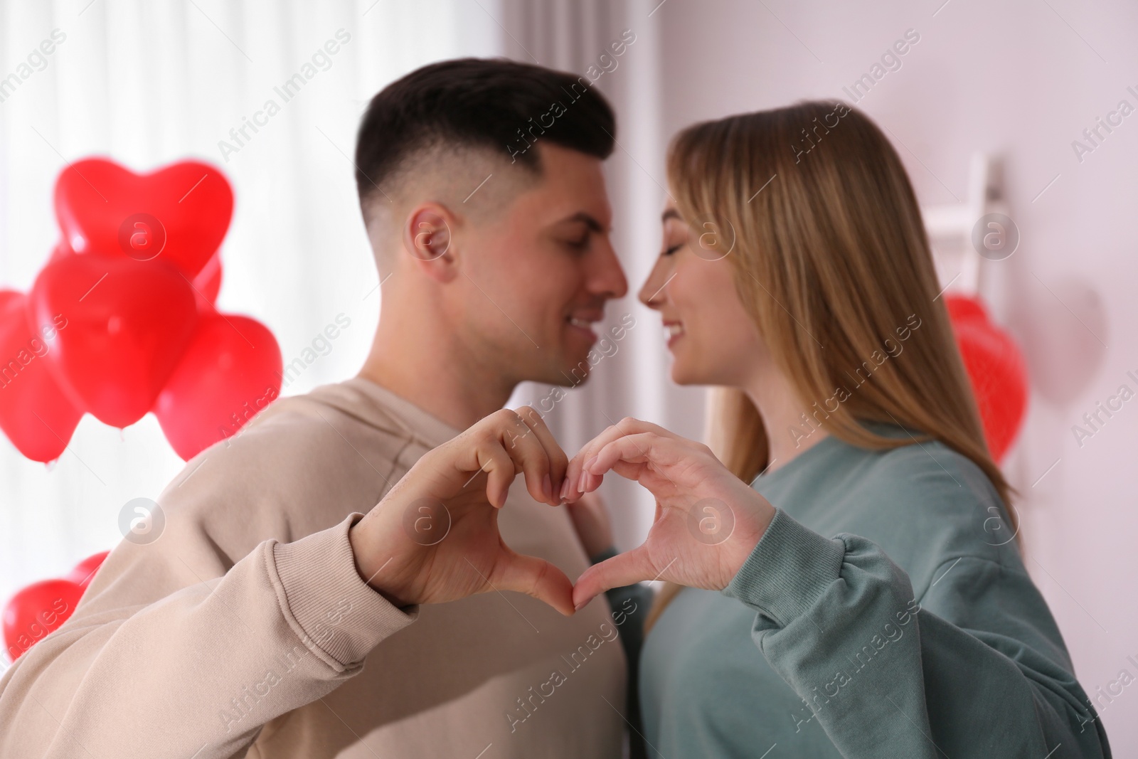 Photo of Lovely couple making heart with hands in room. Valentine's day celebration