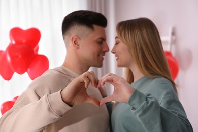 Lovely couple making heart with hands in room. Valentine's day celebration