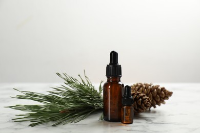 Photo of Pine essential oil, cones and branch on white marble table