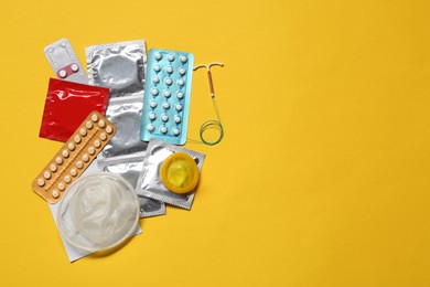 Photo of Contraceptive pills, condoms and intrauterine device on yellow background, flat lay with space for text. Different birth control methods