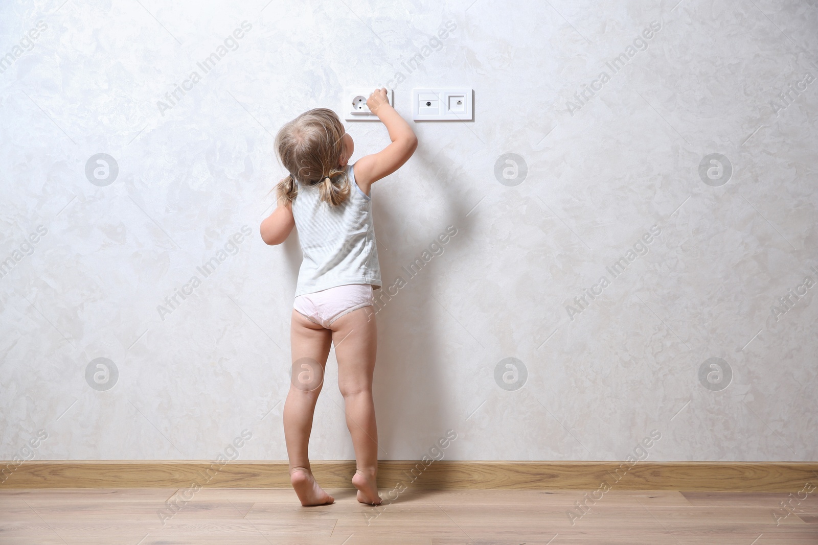 Photo of Little child playing with electrical socket indoors, back view. Dangerous situation