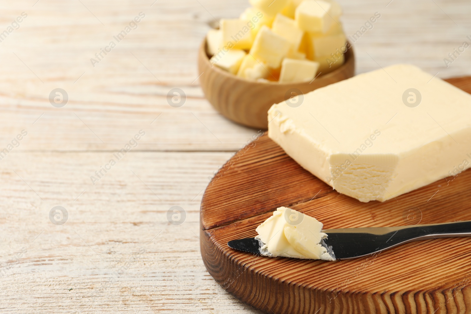 Photo of Tasty butter and knife on light wooden table, closeup. Space for text