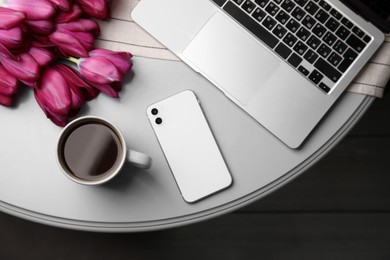 Beautiful tulips, cup of coffee, laptop and smartphone on light gray table indoors, flat lay