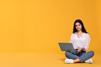 Photo of Student with laptop sitting and pointing at something on yellow background. Space for text