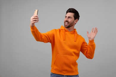 Photo of Smiling man taking selfie with smartphone on grey background