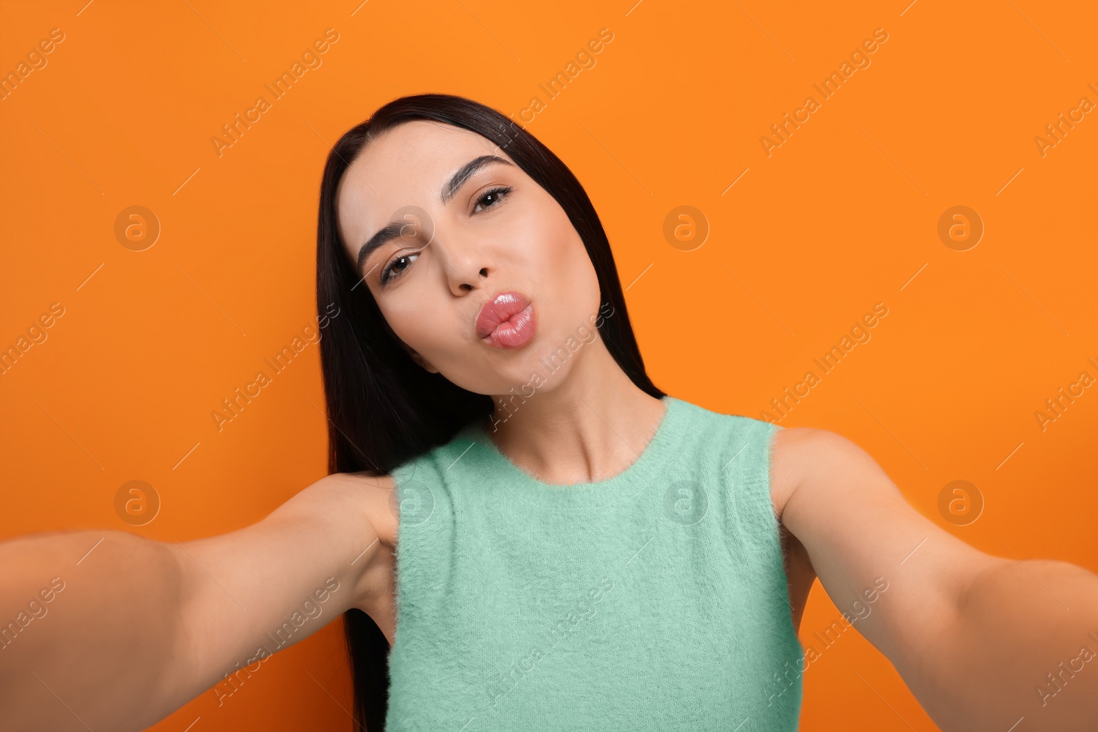 Photo of Beautiful young woman taking selfie while blowing kiss on orange background