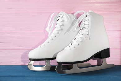 Photo of Pair of white ice skates on blue wooden table against pink background