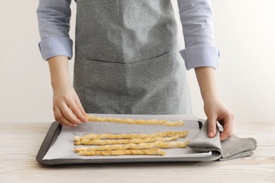 Woman near baking sheet with homemade breadsticks at white wooden table, closeup. Cooking traditional grissini