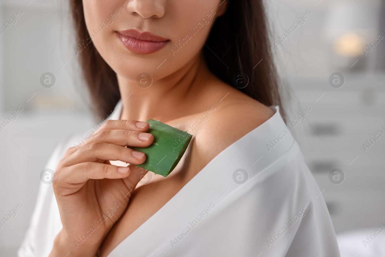 Photo of Young woman applying aloe gel from leaf onto her shoulder indoors, closeup