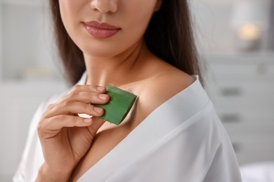 Young woman applying aloe gel from leaf onto her shoulder indoors, closeup