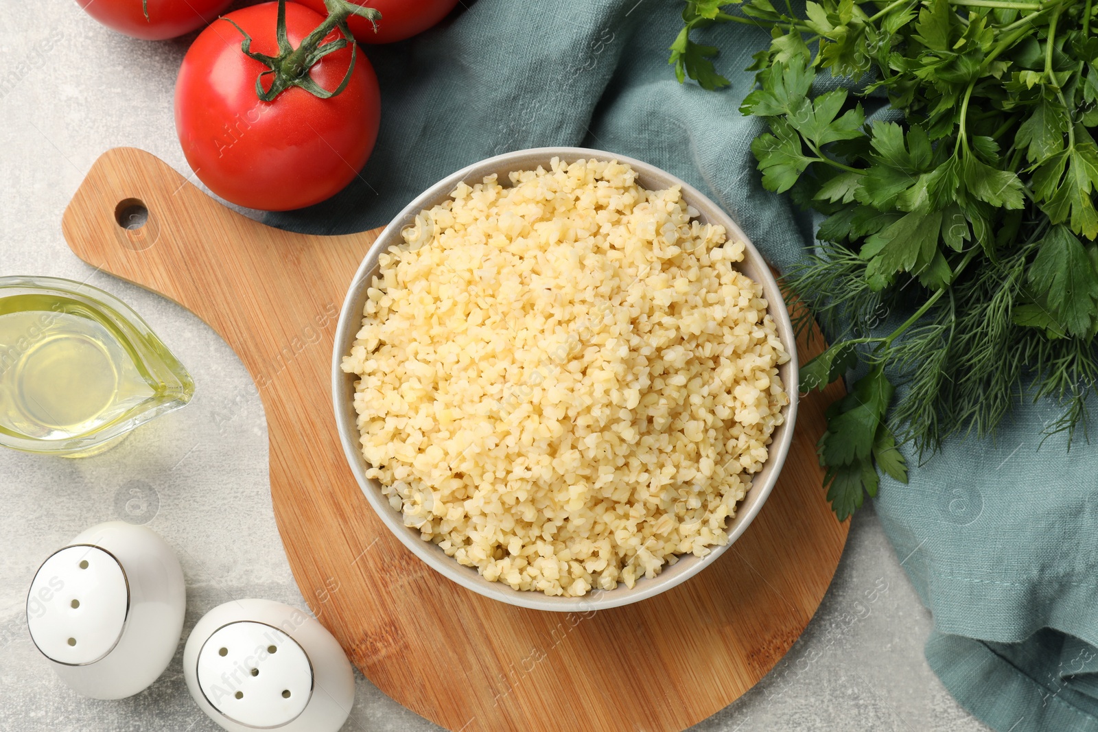 Photo of Delicious bulgur in bowl, tomatoes, oil and spices on table, flat lay