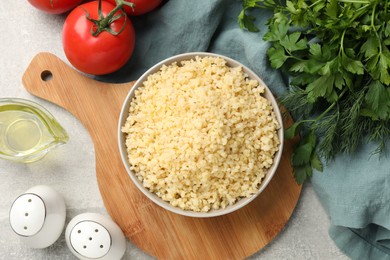 Delicious bulgur in bowl, tomatoes, oil and spices on table, flat lay