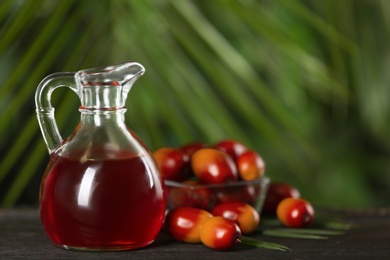 Photo of Palm oil in glass jug, tropical leaf and fruits on wooden table. Space for text