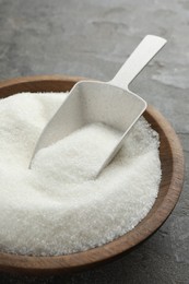 Photo of Granulated sugar in bowl and scoop on grey textured table, closeup