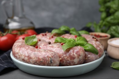 Photo of Raw homemade sausages, basil leaves and peppercorns on grey table, closeup