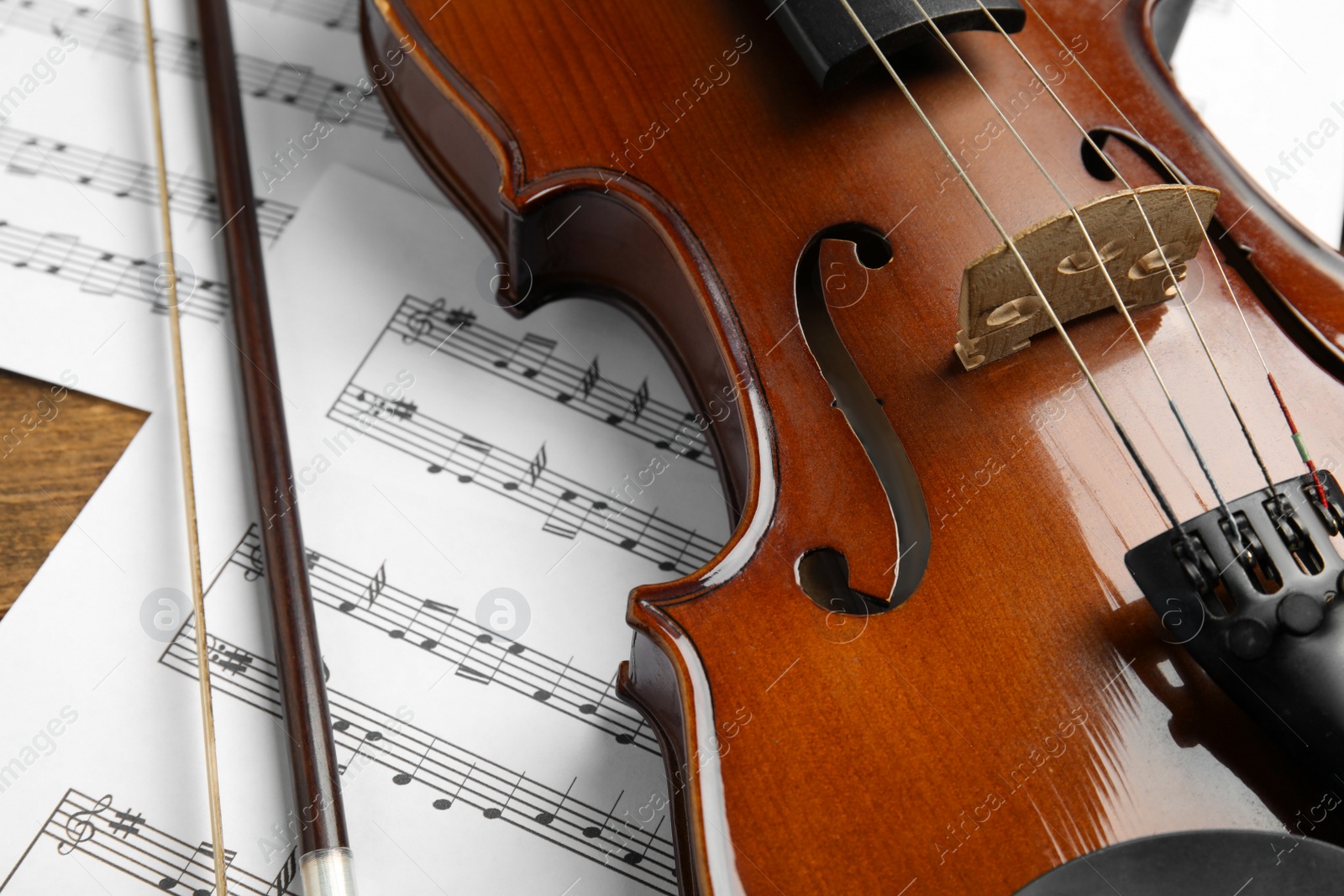 Photo of Beautiful violin, bow and note sheets on table, closeup