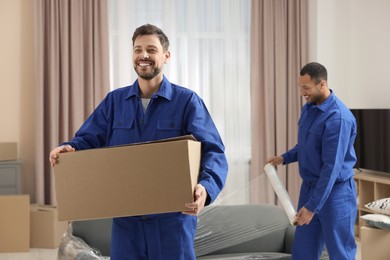 Photo of Male movers with cardboard box and sofa in new house