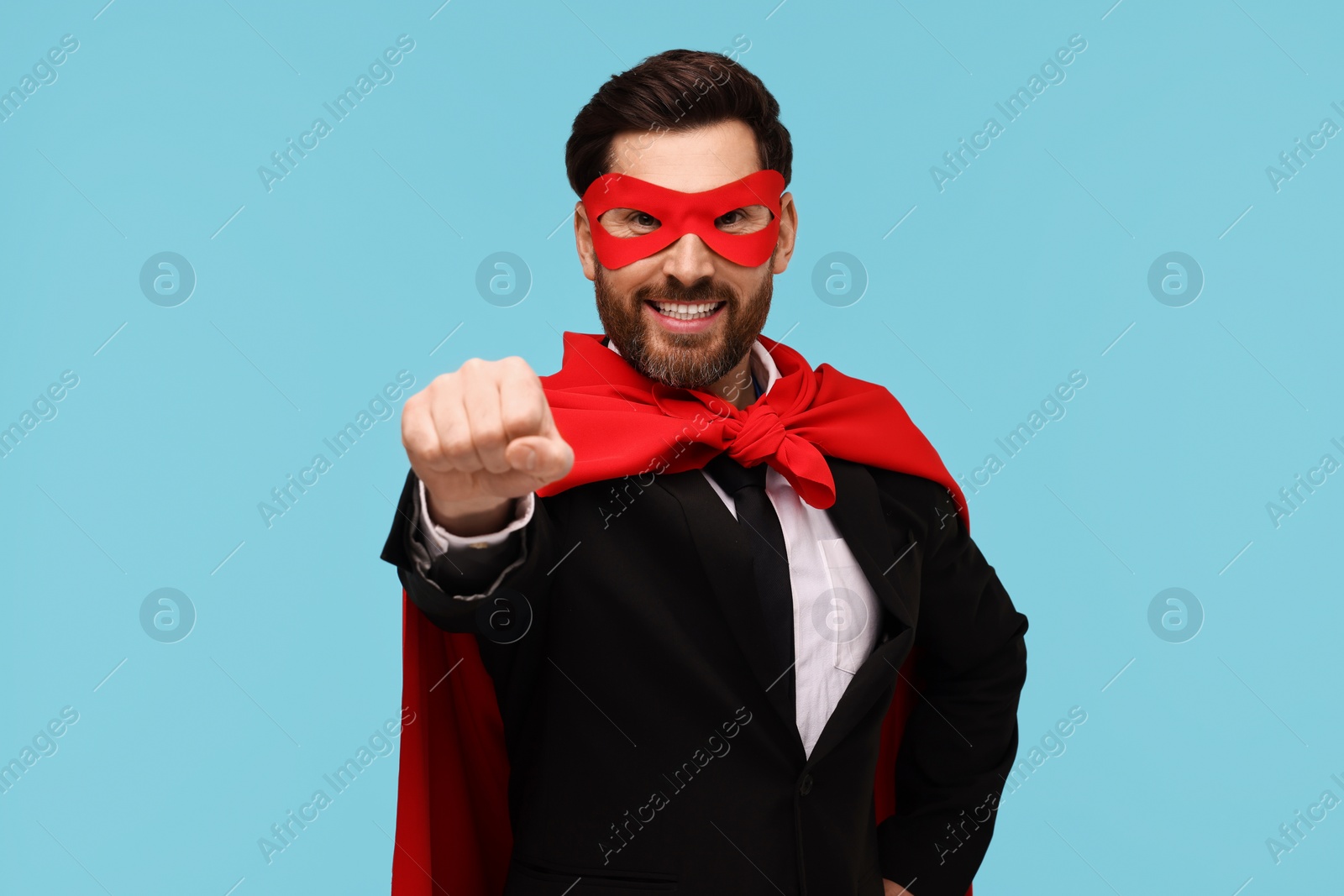 Photo of Businessman wearing red superhero cape and mask on light blue background