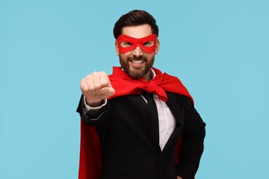 Photo of Businessman wearing red superhero cape and mask on light blue background