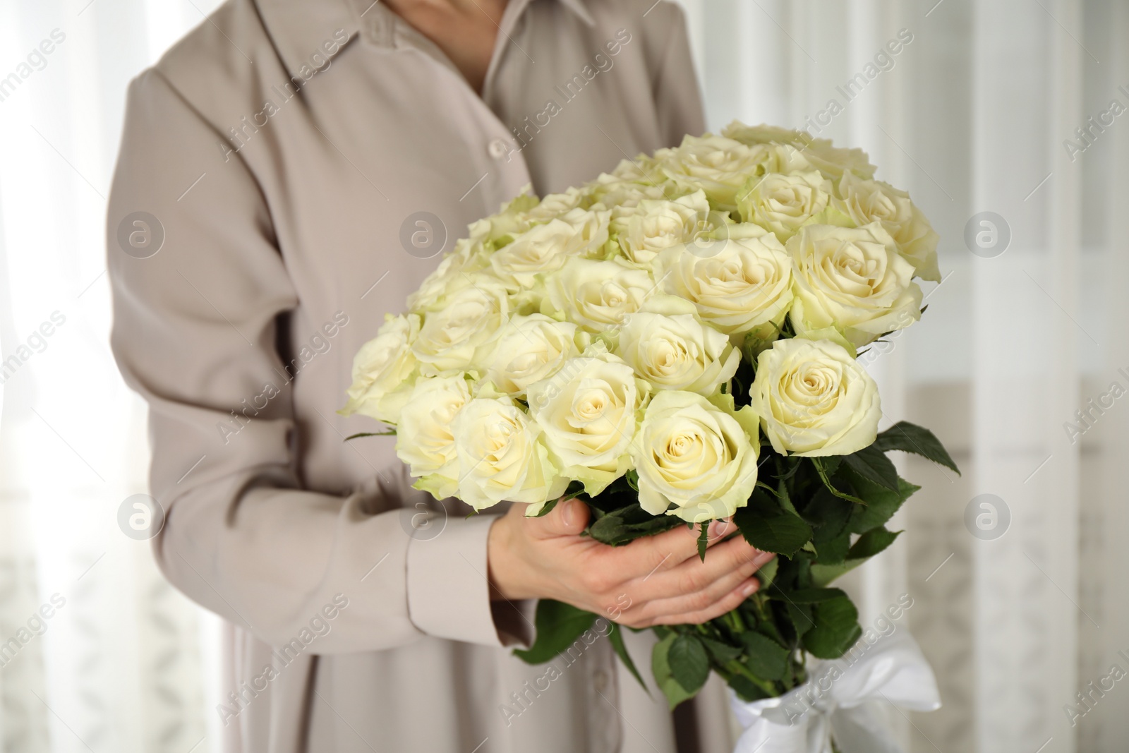 Photo of Woman holding luxury bouquet of fresh roses indoors, closeup