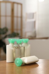 Photo of Mini bottles of cosmetic products and green branch on wooden table against blurred background