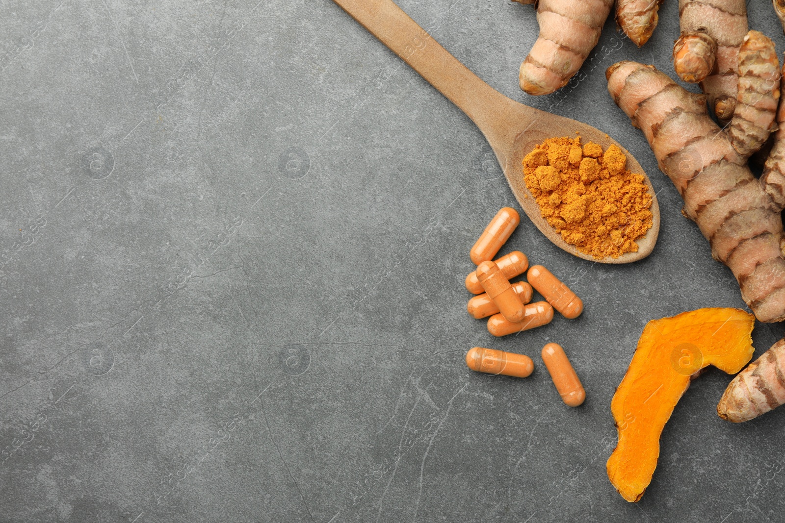 Photo of Aromatic turmeric powder, pills and raw roots on grey table, flat lay. Space for text