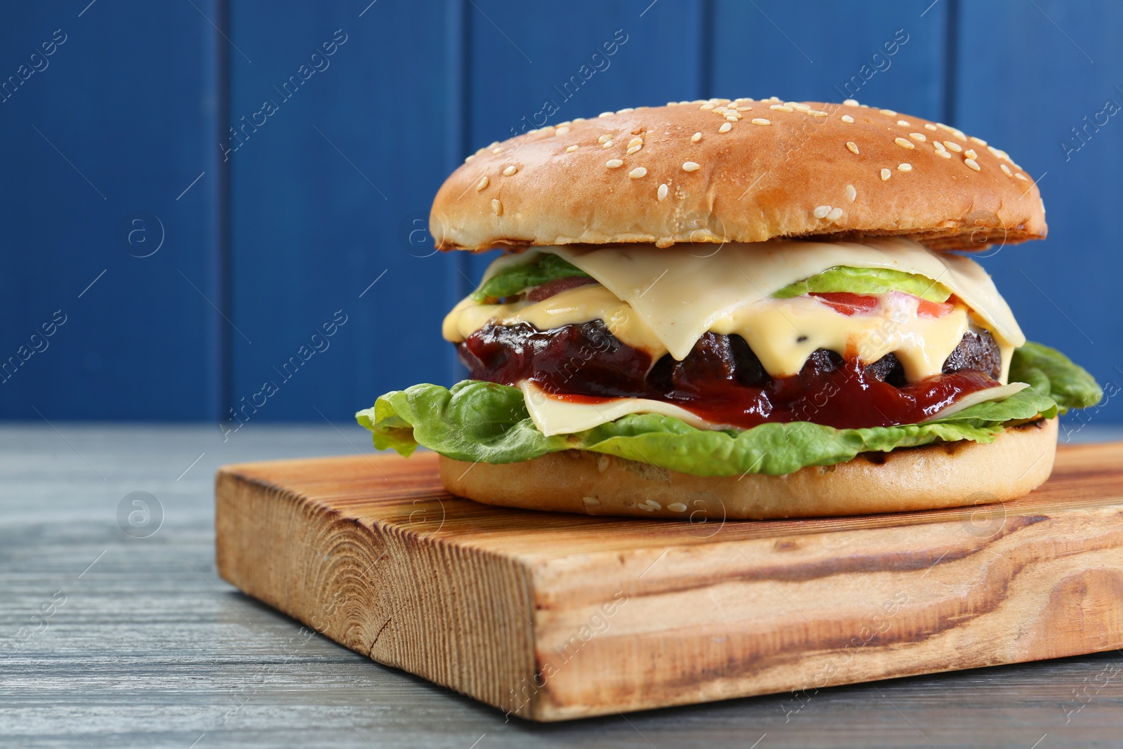 Photo of Tasty homemade cheeseburger with lettuce on grey wooden table, closeup. Space for text